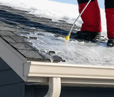 Ice dam removal technician using a steam wand to melt thick ice buildup on a residential roof in Arvada, CO