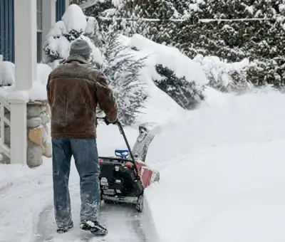 Residential snow removal technician using a snow blower to clear a home driveway and walkway in Arvada, CO